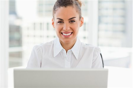 Portrait of a frizzy haired smiling woman working with a laptop in a bright office Stock Photo - Premium Royalty-Free, Code: 6109-06005354