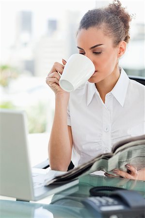 Businesswoman drinking a coffee while holding a newspaper in bright office Stock Photo - Premium Royalty-Free, Code: 6109-06005372