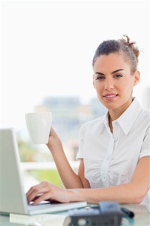 Portrait of a frizzy haired woman with a coffee while tapping on her laptop in a bright office Stock Photo - Premium Royalty-Free, Code: 6109-06005380