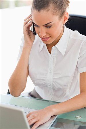 simsearch:6109-06005396,k - Femme d'affaires tannée phoning devant son ordinateur portable dans un bureau lumineux Photographie de stock - Premium Libres de Droits, Code: 6109-06005405