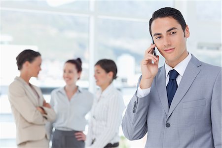 Jeune homme d'affaires sur son téléphone portable avec des associés derrière lui Photographie de stock - Premium Libres de Droits, Code: 6109-06005658