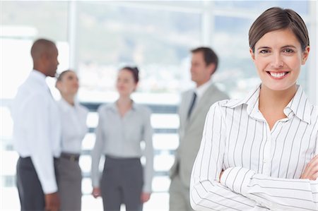 simsearch:6109-06005753,k - Smiling young saleswoman with arms crossed and colleagues behind her Stock Photo - Premium Royalty-Free, Code: 6109-06005699