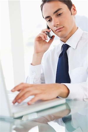 simsearch:6109-06005472,k - Geschäftsmann mit einem Smartphone während der Eingabe von seinem Laptop in ein helles Büro Stockbilder - Premium RF Lizenzfrei, Bildnummer: 6109-06005601