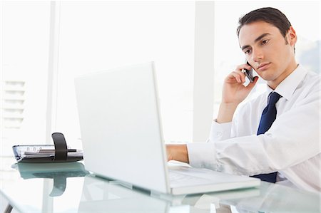 Businessman using a smartphone while looking his laptop in a bright office Foto de stock - Royalty Free Premium, Número: 6109-06005602