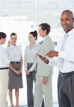 salesman - Smiling young salesman with his tablet pc and colleagues behind him Stock Photo - Premium Royalty-Free, Code: 6109-06005747