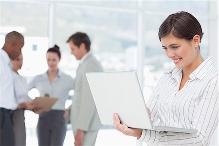 simsearch:6109-06005688,k - Smiling young saleswoman on her laptop with colleagues behind her Foto de stock - Royalty Free Premium, Número: 6109-06005717