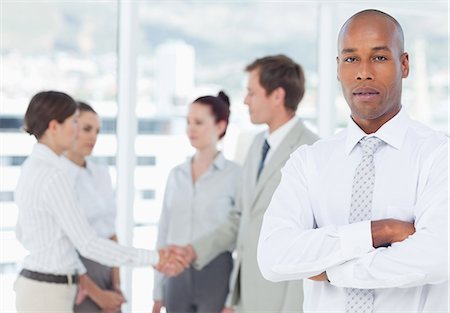 Serious young salesman with arms crossed and colleagues behind him Stock Photo - Premium Royalty-Free, Code: 6109-06005729