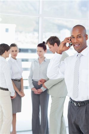 représentant (commerce) - Sourire de jeune vendeur sur son téléphone mobile avec associates derrière lui Photographie de stock - Premium Libres de Droits, Code: 6109-06005739