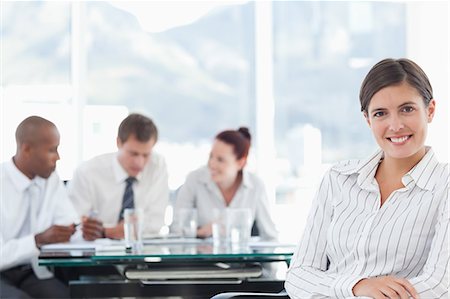 simsearch:6109-06005806,k - Smiling young businesswoman with colleagues behind her holding a meeting Stock Photo - Premium Royalty-Free, Code: 6109-06005862