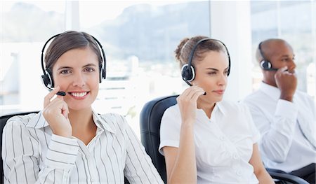 Smiling young telephone hotline employee sitting next to her colleagues Stock Photo - Premium Royalty-Free, Code: 6109-06005807