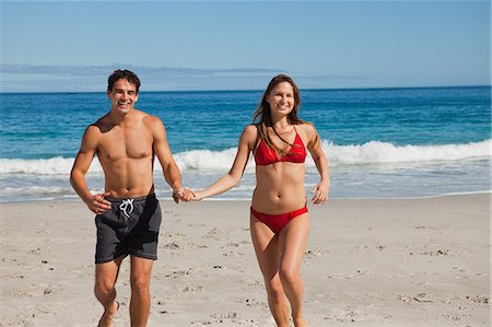 Happy lovers in swimsuit holdings hands while running on the beach Stock Photo - Premium Royalty-Free, Code: 6109-06005943