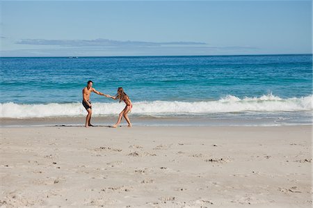 Lovers in swimsuit pulling by the hand on the beach Stock Photo - Premium Royalty-Free, Code: 6109-06005941