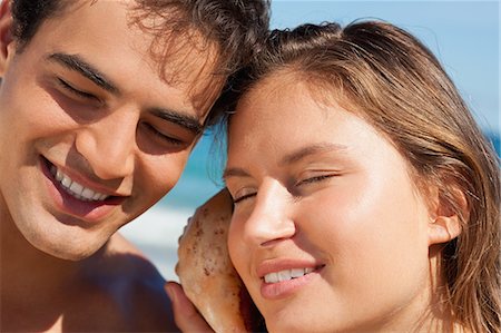 Close-up of a couple listening to a seashell with the sea in background Stock Photo - Premium Royalty-Free, Code: 6109-06005989