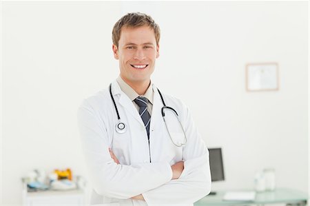 simsearch:6109-06006507,k - Smiling young doctor with arms folded in his examination room Fotografie stock - Premium Royalty-Free, Codice: 6109-06006343