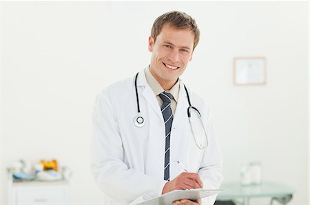 simsearch:6109-06006352,k - Smiling young doctor taking notes in his examination room Foto de stock - Sin royalties Premium, Código: 6109-06006346