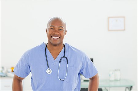 doctor uniform - Smiling male doctor in scrubs standing in examination room Foto de stock - Sin royalties Premium, Código: 6109-06006371