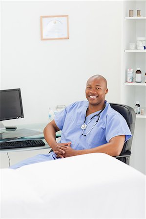 folded hands - Smiling male doctor in scrubs sitting in his examination room Foto de stock - Sin royalties Premium, Código: 6109-06006375