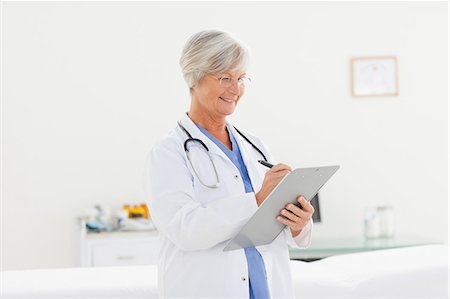 simsearch:6109-06006352,k - Smiling mature doctor taking notes on clipboard Foto de stock - Sin royalties Premium, Código: 6109-06006316