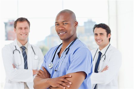 simsearch:6109-06005901,k - Three smiling doctors with their arms crossed standing in front of a window Fotografie stock - Premium Royalty-Free, Codice: 6109-06006546
