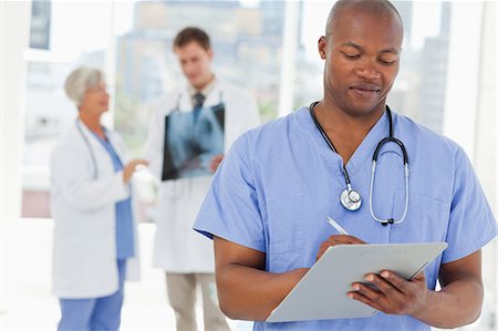 Doctor in scrubs with clipboard and two colleagues behind him Stock Photo - Premium Royalty-Free, Code: 6109-06006511