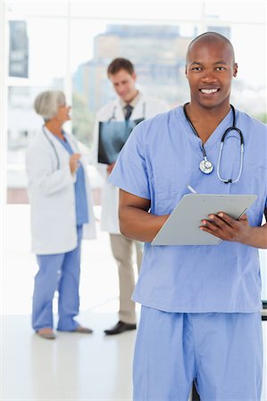 simsearch:6109-06006507,k - Smiling doctor with his clipboard and two colleagues behind him Fotografie stock - Premium Royalty-Free, Codice: 6109-06006514