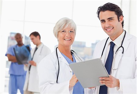simsearch:6109-06006507,k - Smiling doctors with clipboard and two colleagues behind them Fotografie stock - Premium Royalty-Free, Codice: 6109-06006530