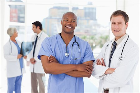simsearch:6109-06006507,k - Smiling doctors with arms folded and two colleagues behind them Fotografie stock - Premium Royalty-Free, Codice: 6109-06006536