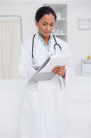 Young serious doctor writing on a clipboard while standing up in a hospital room Stock Photo - Premium Royalty-Free, Code: 6109-06006763