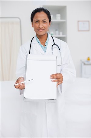 Young doctor looking at the camera while pointing her clipboard with her pen Stock Photo - Premium Royalty-Free, Code: 6109-06006768