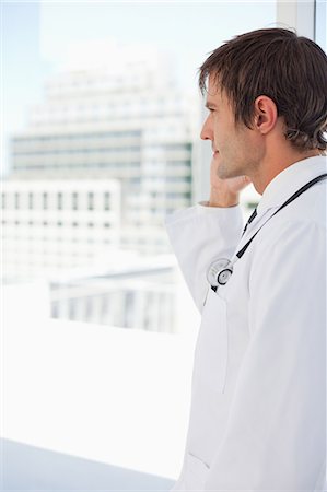 Vue latérale d'un médecin avec son téléphone portable en face d'une fenêtre Photographie de stock - Premium Libres de Droits, Code: 6109-06006782