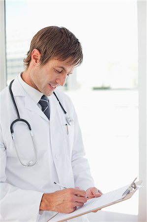 simsearch:6109-06006944,k - Smiling doctor working with his clipboard while standing in front of a window Foto de stock - Sin royalties Premium, Código: 6109-06006797