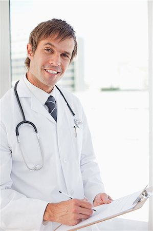 simsearch:6109-06006944,k - Smiling surgeon writing on his clipboard while standing upright in front of a window Foto de stock - Sin royalties Premium, Código: 6109-06006798