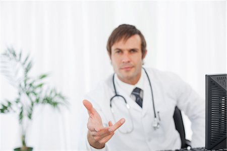 Hand extended by a serious doctor sitting behind his desk Stock Photo - Premium Royalty-Free, Code: 6109-06006850