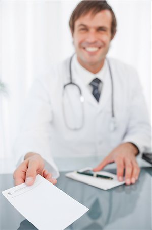 doctor with prescription - Prescription being held out by a smiling doctor sitting at his desk Stock Photo - Premium Royalty-Free, Code: 6109-06006858