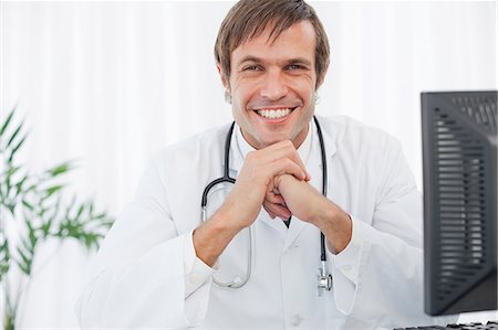 doctors relaxing - Smiling doctor sitting behind his desk while placing his elbows on his desk Stock Photo - Premium Royalty-Free, Code: 6109-06006861