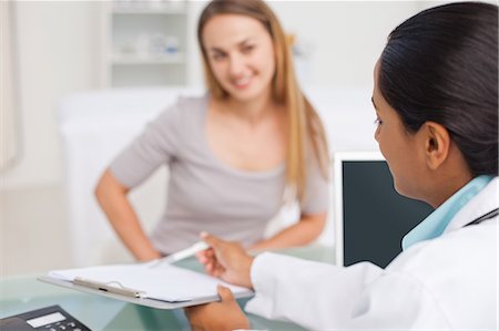 doctor at desk with patient - Rear view of a doctor pointing at her clipboard while talking to her patient Stock Photo - Premium Royalty-Free, Code: 6109-06006883