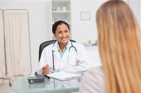 explaining - Doctor looking at her patient while sitting at her desk and writing on her clipboard Stock Photo - Premium Royalty-Free, Code: 6109-06006884