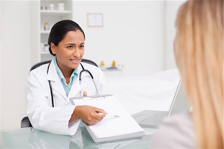 doctor at desk with patient - Relaxed doctor showing her clipboard to a patient Stock Photo - Premium Royalty-Free, Code: 6109-06006889