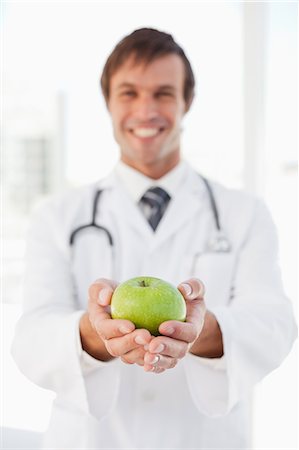 simsearch:6109-06006928,k - Un médecin heureux tient une pomme verte en face d'une fenêtre Photographie de stock - Premium Libres de Droits, Code: 6109-06006808