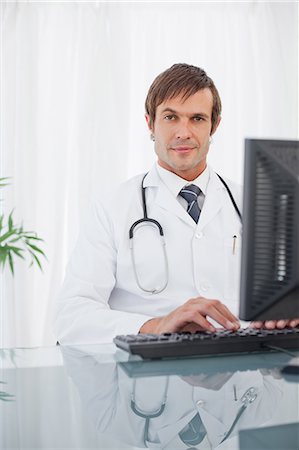 Surgeon raising an eyebrow while sitting at his desk and working on a computer Stock Photo - Premium Royalty-Free, Code: 6109-06006821