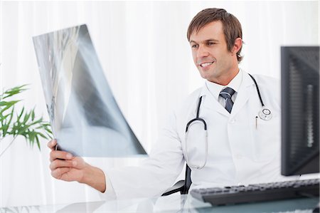 examen de pecho - Smiling doctor sitting behind his desk while holding a chest x-ray Foto de stock - Sin royalties Premium, Código: 6109-06006824