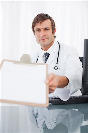 simsearch:6109-06006944,k - Doctor showing his clipboard while sitting at the desk and looking at the camera Foto de stock - Sin royalties Premium, Código: 6109-06006834