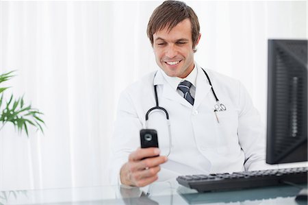 Smiling doctor raising an eyebrow while looking at his mobile phone Stock Photo - Premium Royalty-Free, Code: 6109-06006838