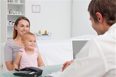 Young woman holding her little baby while smiling and looking at the doctor Stock Photo - Premium Royalty-Free, Code: 6109-06006947