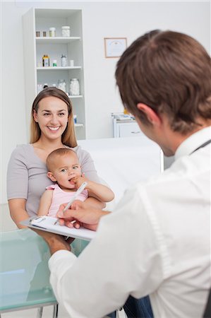 doctor holding a baby - Smiling mother holding her baby in front of the doctor who is using his clipboard Stock Photo - Premium Royalty-Free, Code: 6109-06006952