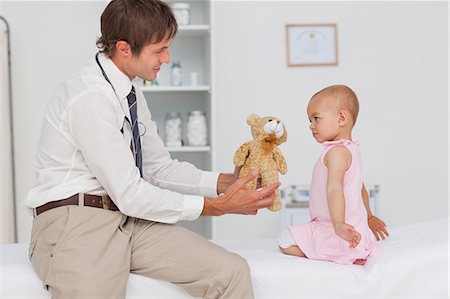 doctor holding a baby - Little baby looking at a teddy bear offered by the practitioner Stock Photo - Premium Royalty-Free, Code: 6109-06006964