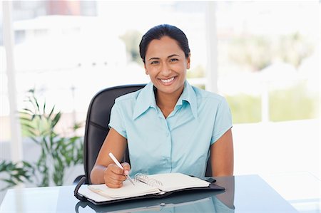 simsearch:6109-06006973,k - Smiling secretary looking at the camera while writing on a diary Stock Photo - Premium Royalty-Free, Code: 6109-06006973