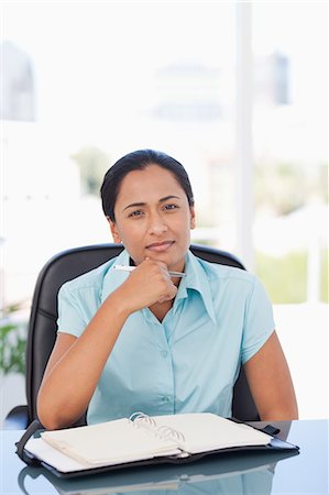 day planner - Relaxed secretary looking at the camera while sitting at a desk and holding her pen Stock Photo - Premium Royalty-Free, Code: 6109-06006970