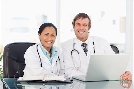 simsearch:6109-06006905,k - Smiling doctor sitting at the desk while being accompanied by his co-worker Stock Photo - Premium Royalty-Free, Code: 6109-06006997