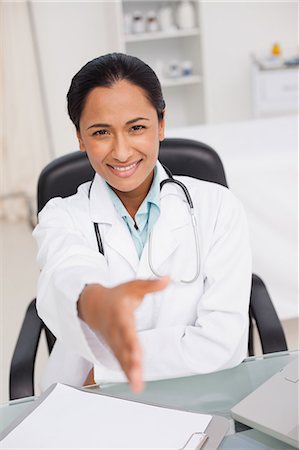 simsearch:6109-06006911,k - Smiling doctor offering a handshake while sitting in her medical office Fotografie stock - Premium Royalty-Free, Codice: 6109-06006903